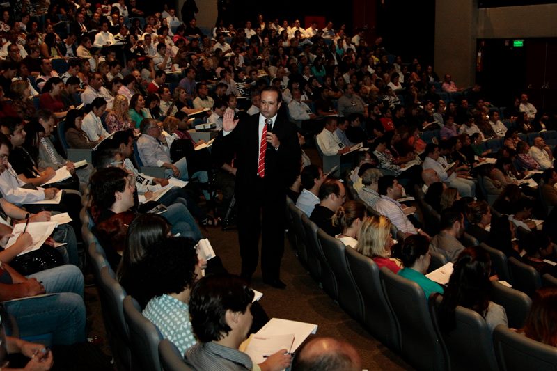 Palestrante para evento corporativo interagindo com o público em um auditório lotado